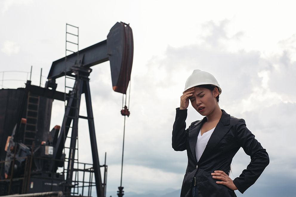 Female engineer standing with working oil pumps with a white sky